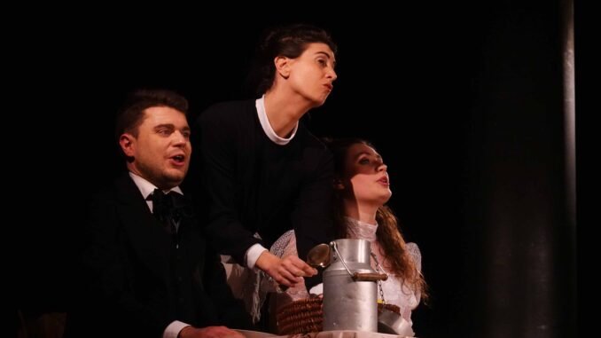 photo de 2 femmes et 1 homme devant une table sur laquelle est posé un pot à lait, le tout sur fond noir