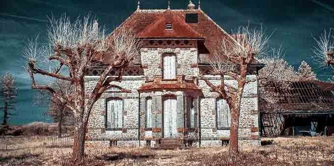 photo d'une vieille maison avec 1 étage derrière deux arbres sans feuilles